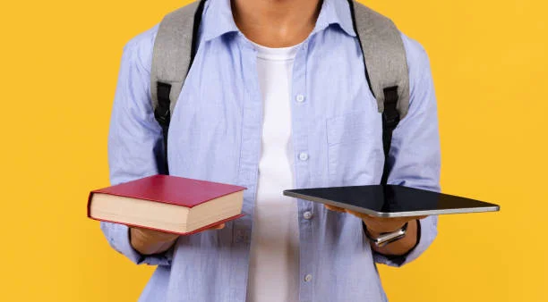 Student male comparing book with tablet